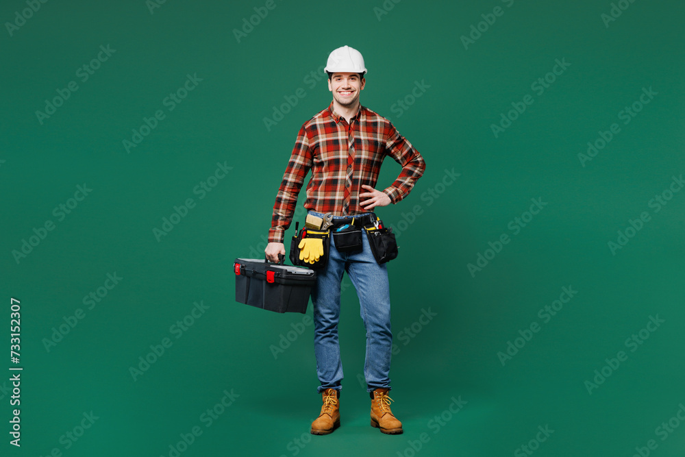 Wall mural full body smiling young employee laborer man wear red shirt hardhat hat work hold toolbox isolated o