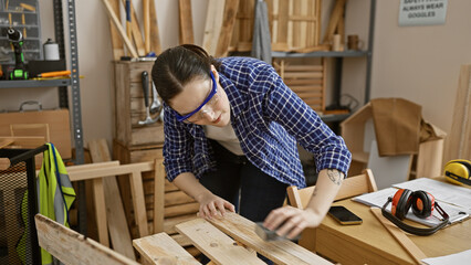 A focused woman in safety glasses working with wood in a carpentry workshop. © Krakenimages.com