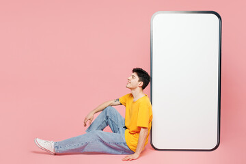 Full body young man he wears yellow t-shirt casual clothes sit near big huge blank screen mobile...