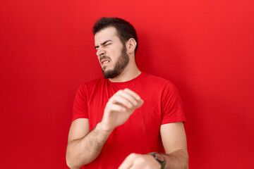 Young hispanic man wearing casual red t shirt disgusted expression, displeased and fearful doing disgust face because aversion reaction.
