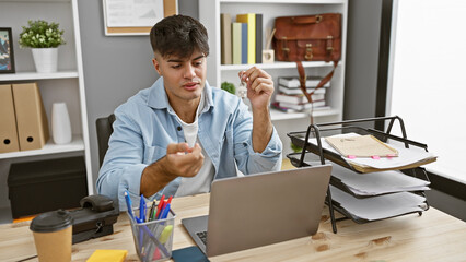 Portrait of a young handsome hispanic man, a relaxed but serious business worker, immersed in online work on his laptop at the office desk, achieving success in his professional job indoors.