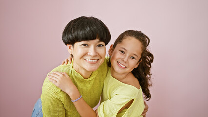 Confident mother and daughter sharing a lovely, happy hug while smiling and standing together over an isolated pink background, expressing a casual lifestyle full of fun, joy and positive vibes.