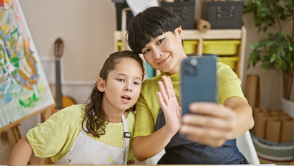 Mother-daughter bonding, woman artist teacher and young girl student draw together on notebook during indoor art lesson, smiling and sharing via video call in vibrant studio space