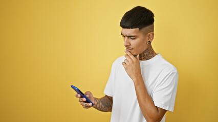 Cool tattooed young latin man concentrates on texting, his serious expression illuminated by...