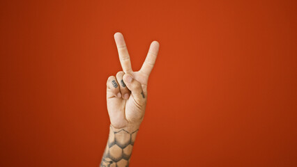 Man's hand amped up with v for victory sign over isolated red wall, man - male adult hispanic, tattooed good gesture, no people around