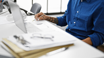 Tattooed professional hispanic man, a dynamic worker sitting at his indoor office desk, hands busy...