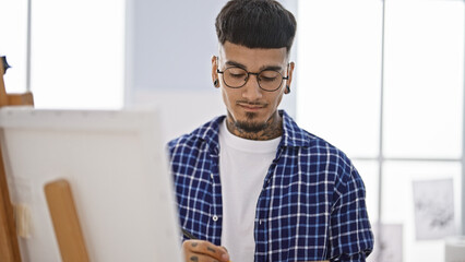 Talented young latin man, a budding tattooed artist, immersed in his art, drawing passionately at his canvas in the indoors art studio