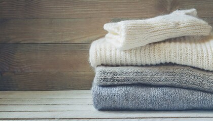 Obraz na płótnie Canvas stack of knitted winter clothes on wooden background sweaters space for text toning image