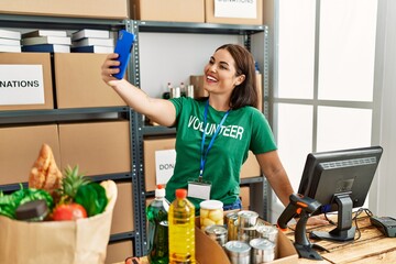 Young beautiful hispanic woman volunteer make selfie by smartphone standing at charity center