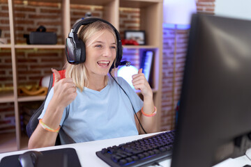 Young caucasian woman playing video games wearing headphones success sign doing positive gesture...