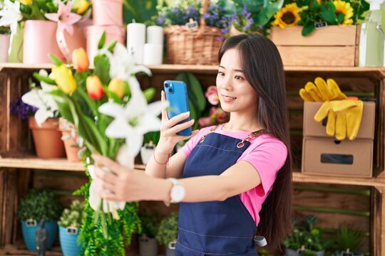Young chinese woman florist make photo to flowers by smartphone at flower shop