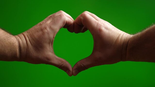 With the help of two hands, make an image of a heart on a green background.