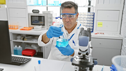 Fototapeta na wymiar A mature male scientist examining a chemical in a flask within a modern laboratory setting.