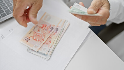 A man counts singaporean dollars in an office, suggesting business, finance, and economy themes.