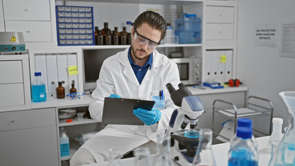 Young hispanic man scientist writing report sitting at laboratory