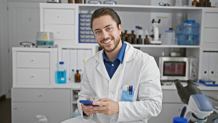Fototapeta na wymiar Young hispanic man scientist smiling confident using smartphone at laboratory