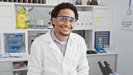 Smiling man wearing lab coat and safety goggles in scientific laboratory setting - obrazy, fototapety, plakaty
