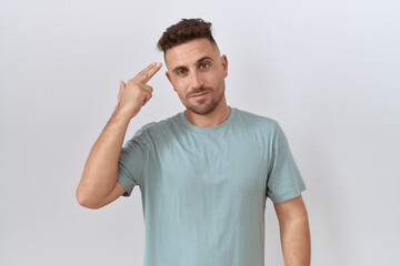 Hispanic man with beard standing over white background shooting and killing oneself pointing hand and fingers to head like gun, suicide gesture.