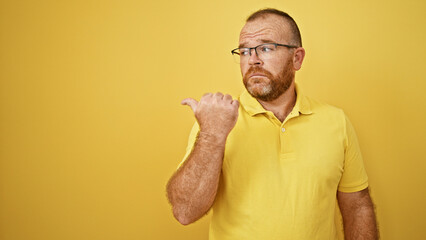 Caucasian man pointing to the side with serious face over isolated yellow background