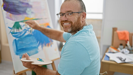 Attractive middle-aged caucasian man confidently enjoying his hobby, smiling as he draws a piece of...