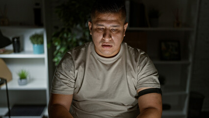 Young latin man at work, a portrait of serious business worker, confidently sitting in his dim...