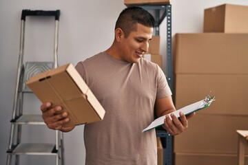 Young latin man ecommerce business worker reading document holding package at office
