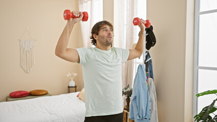 A young man lifts weights in a well-lit bedroom, showcasing fitness and a casual home workout...