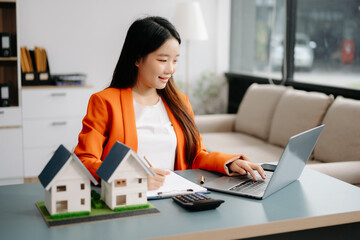 Young real estate agent worker working with laptop and tablet at table in office and small house...