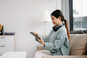 Asian woman using the smartphone and tablet on the sofa at home office.