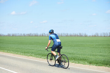 Obraz premium An athlete in cycling or triathlon competitions. A man in a bicycle uniform and helmet. Check-in on the highway