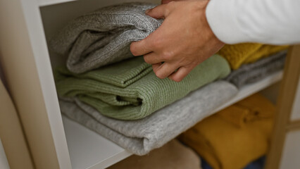 A man organizes sweaters in a wardrobe, indicating tidiness in a home interior with a focus on...