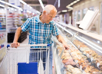 Old age man buys cooked takeaway food in supermarket cooking department