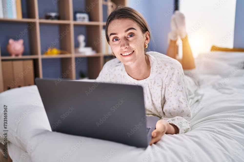 Wall mural Young caucasian woman using laptop lying on bed at bedroom