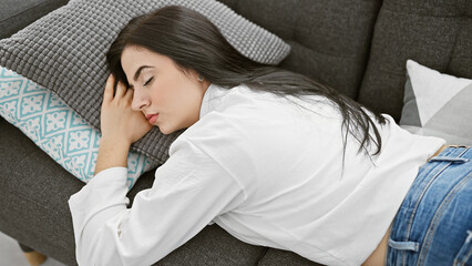 A serene hispanic woman rests on a sofa in a cozy living room, embodying tranquility and comfort.