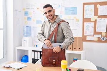 Young hispanic man business worker smiling confident holding laptop of briefcase at office