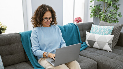 Hispanic woman using laptop comfortably in her modern living room at home
