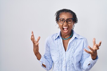 African woman with dreadlocks standing over white background wearing glasses crazy and mad shouting...