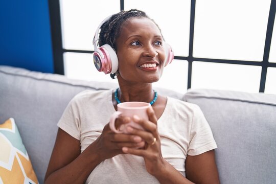 Middle age african american woman listening to music drinking coffee at home