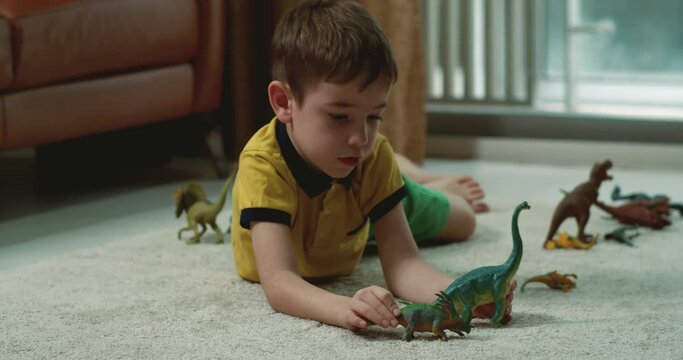 Happy little boy explain paleontology having fun at home together. Loving young adult sister and cute preschool child brother talking playing dinosaurs toys sit on warm floor. 4K