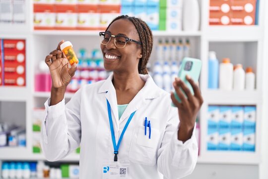 African american woman pharmacist holding pills bottle using smartphone at pharmacy