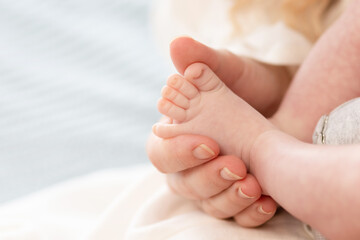 the parent's hand holds the baby's small leg, light close-up photo. family concept. background with...