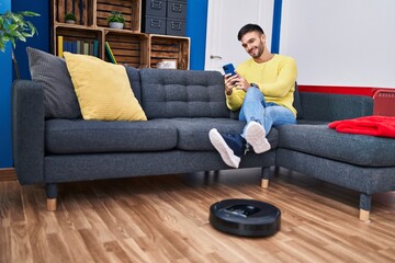 Obraz premium Young hispanic man cleaning floor using cleaner vacuum robot at home