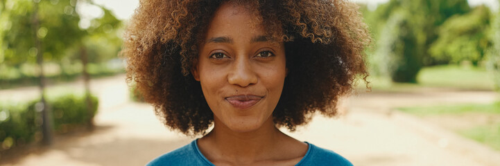 Close-up of young smiling woman with curly hair wearing blue t-shirt posing for the camera in the...