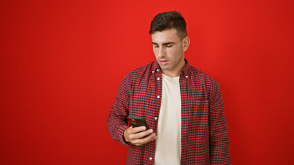 Young hispanic man using smartphone over isolated red background