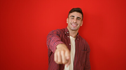 Confident young hispanic man, joy radiating from his smile, pointing a finger at you, the camera,...