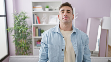 Young hispanic man standing with serious expression at home