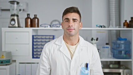 Young hispanic man scientist standing with serious face at laboratory