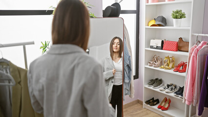 Young woman trying on jacket in a modern dressing room, with mirror and shelves of shoes and bags.
