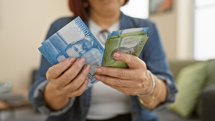 Hispanic woman comparing chilean pesos with american dollars indoors, implying financial...