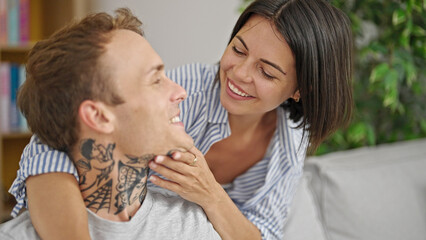 Beautiful couple hugging each other sitting on sofa smiling at home